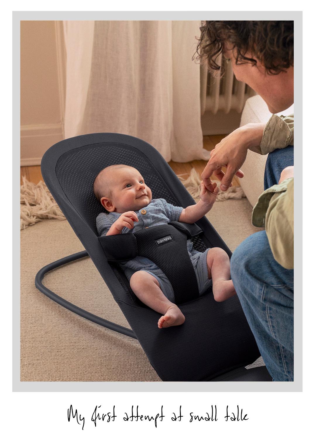 A baby in a bouncer seat reaches for an adult's hand. A handwritten caption below reads, "My first attempt at small talk."