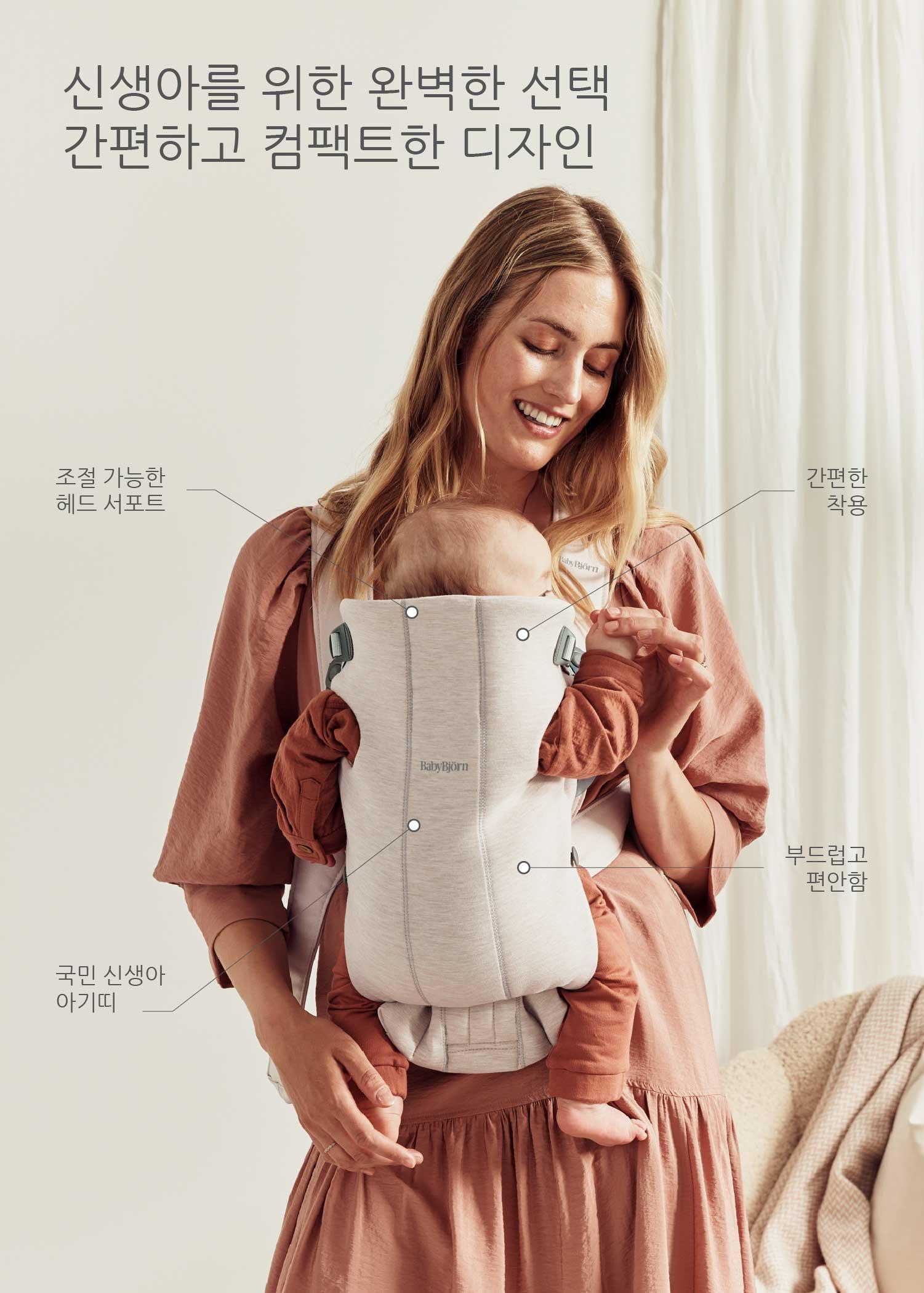 A smiling woman wearing a pink dress carries a baby in a beige baby carrier. Korean text describes features of the carrier.