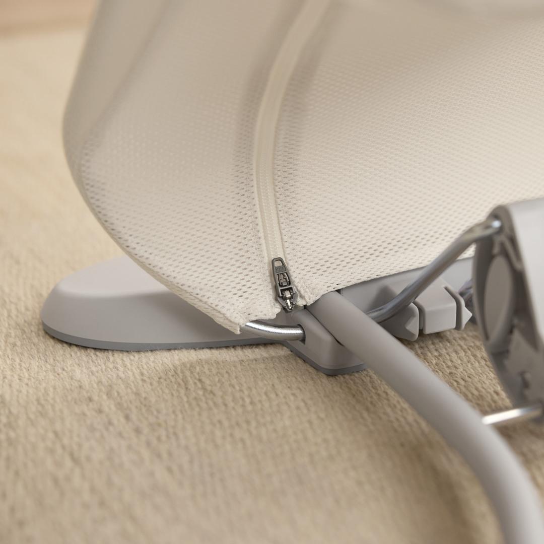 Close-up of a beige fabric canopy with a visible zipper and a metal frame, resting on a textured light brown surface.