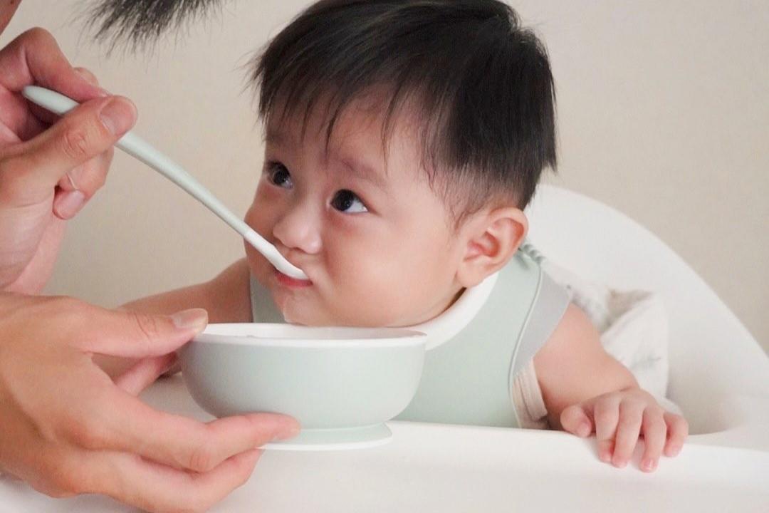 A baby in a high chair being fed with a spoon, looking intently at the food.