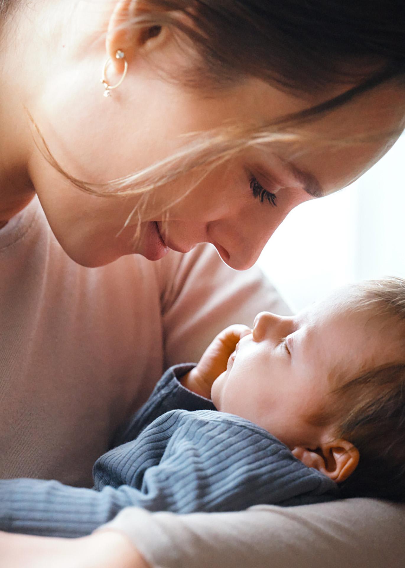 A woman gently gazes at a sleeping baby in her arms, creating a tender and intimate moment.