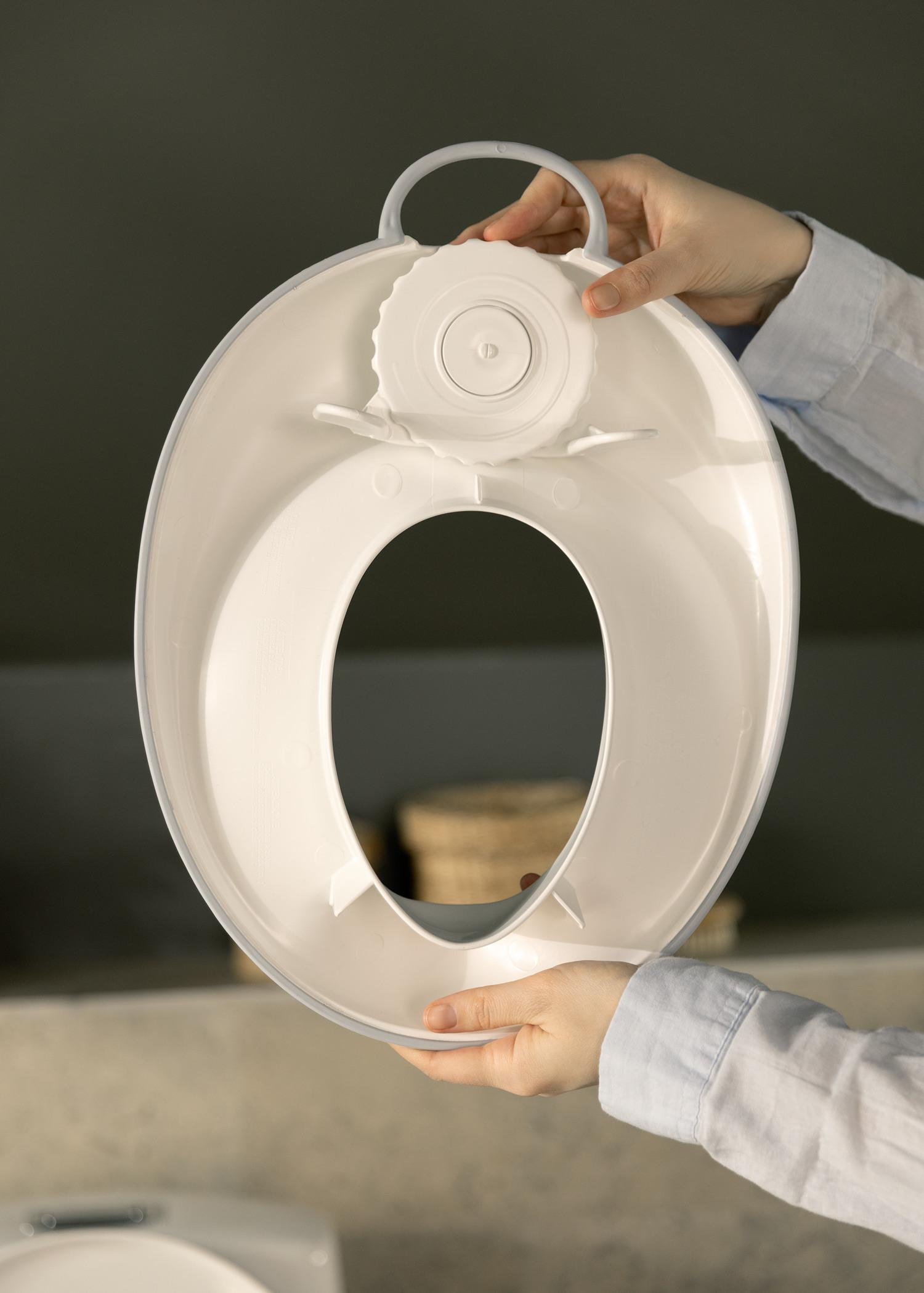 Hands holding a white detachable toilet seat lid with a circular handle, against a dark background.
