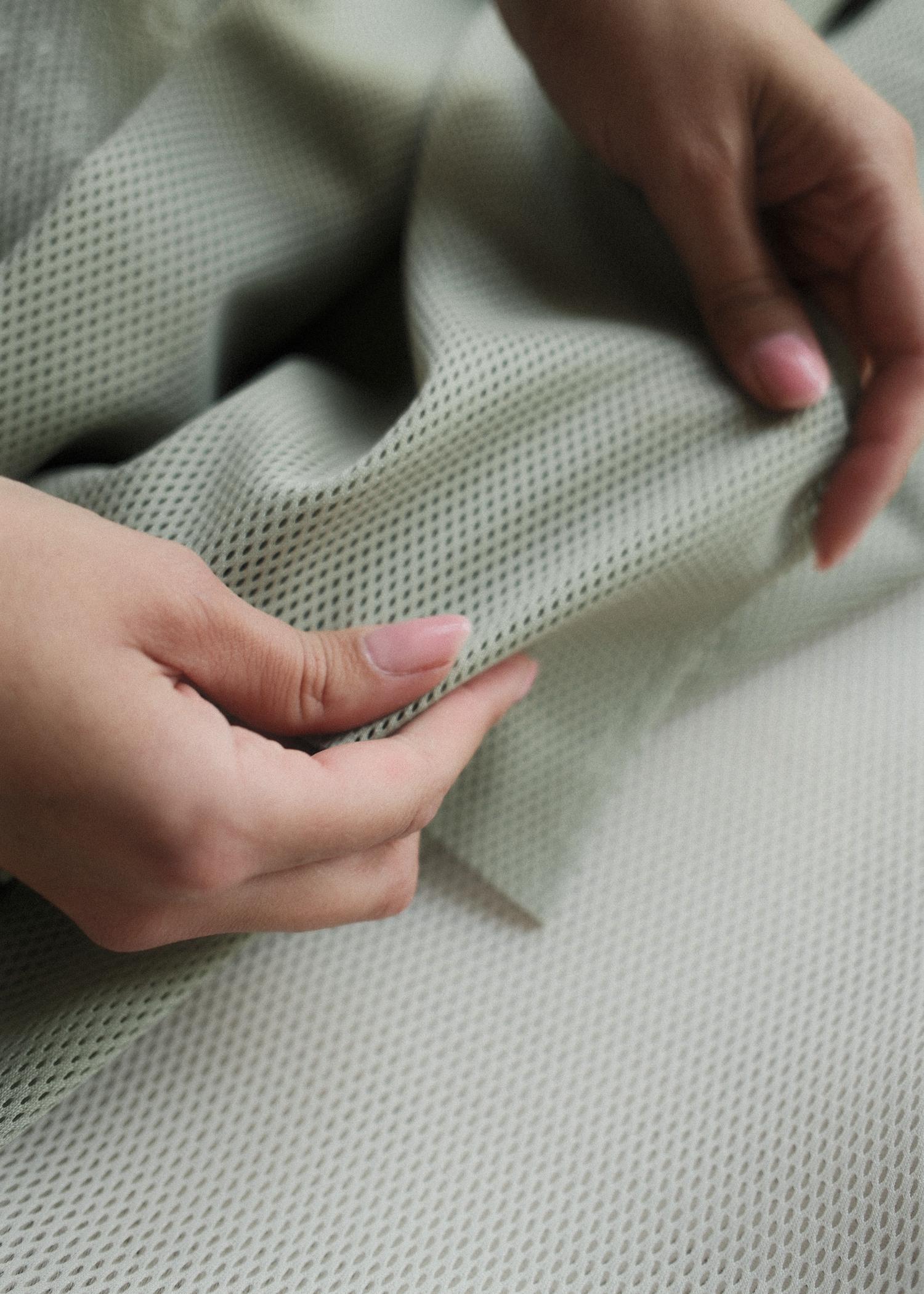 Hands holding and feeling a piece of light green, textured mesh fabric.