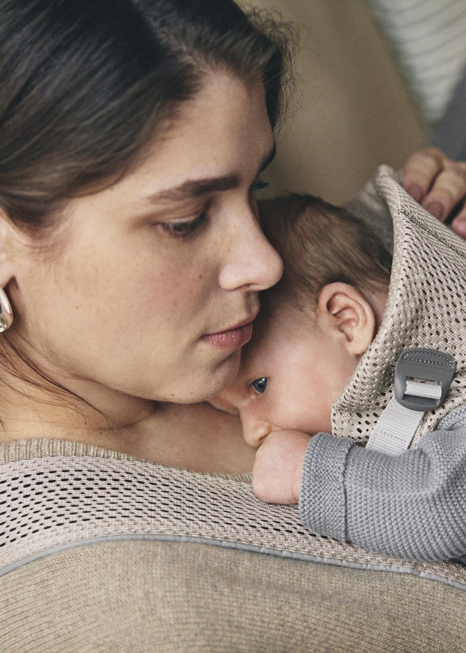 A woman gently holds a baby close to her chest, both wrapped in cozy knitwear, conveying warmth and tenderness.