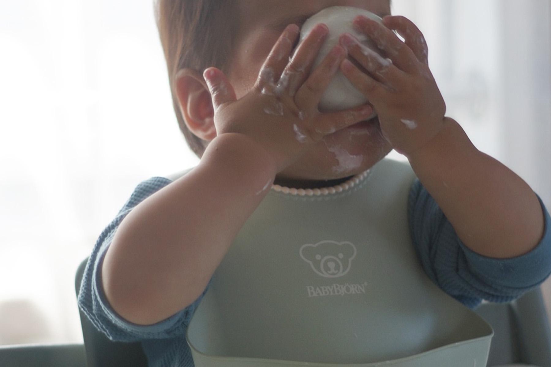 A toddler wearing a bib plays with a food item, covering their face and hands with it, creating a playful and messy scene.