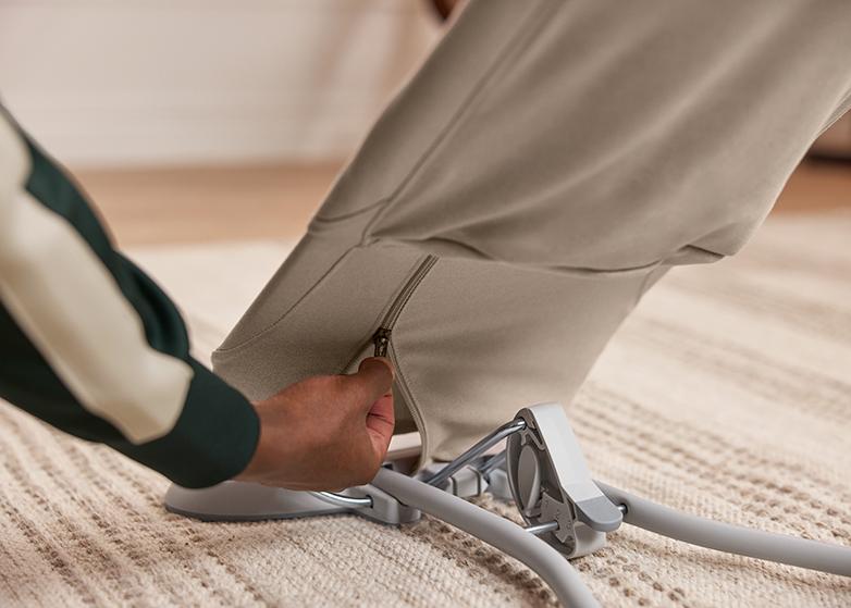 A hand unzipping a beige fabric cover on a baby bouncer on a cream carpet.